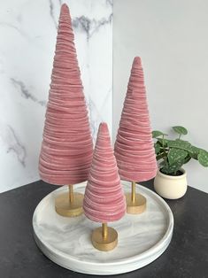 three pink christmas trees sitting on top of a white plate next to a potted plant