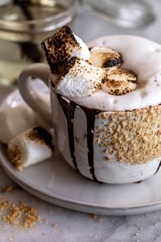 a cup filled with hot chocolate and marshmallows on top of a plate