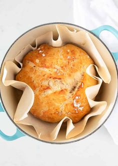 a loaf of bread sitting in a pot on top of a white tablecloth with blue handles