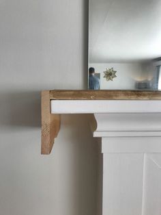 a mirror sitting on top of a wooden shelf next to a white fireplace mantel