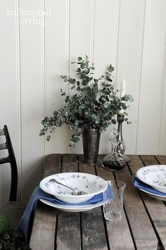 two plates on a wooden table with flowers in a vase next to it and another plate sitting on the table