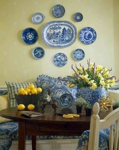 a dining room table with blue and white plates on the wall above it, along with yellow flowers