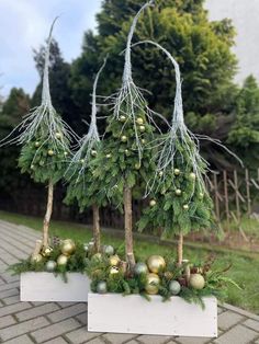 three white planters filled with green and gold ornaments on top of a brick walkway