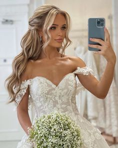 a woman in a wedding dress taking a selfie with her cell phone while holding a bouquet of baby's breath