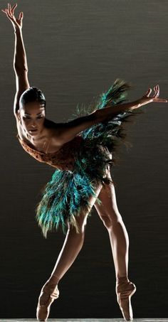 a woman in a green feathered skirt is doing a ballet move with her arms outstretched