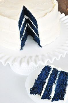 a blue cake with white frosting on a plate next to a slice cut out