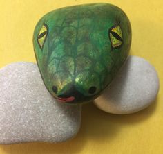 a close up of a rock with a green snake painted on it's face