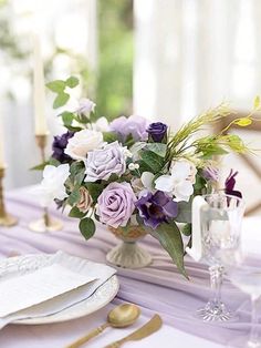 the table is set with purple and white flowers, silverware, and gold place settings