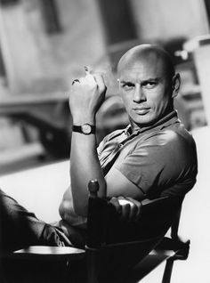 a black and white photo of a man sitting in a chair with his hand on his chin