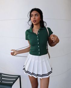 a woman in a green shirt and white pleated skirt standing next to a chair