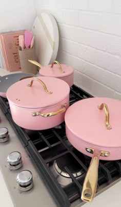 three pink pots and pans sitting on top of an oven burner with gold handles