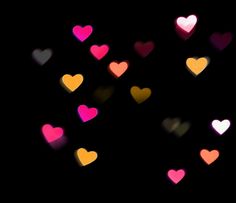 many different colored hearts floating in the air on a black background with blurry lights