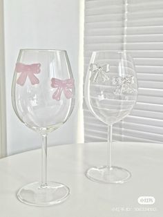 two wine glasses sitting next to each other on top of a white table with blinds in the background