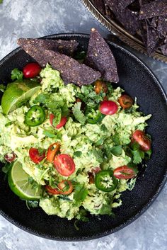 a black plate topped with guacamole and tortilla chips next to an avocado