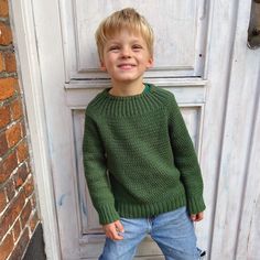 a little boy standing in front of a white door wearing a green sweater and jeans