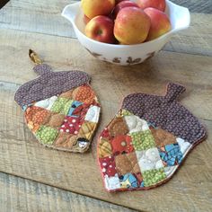 two oven mitts sitting on top of a wooden table next to a bowl of apples