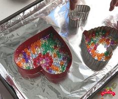 two tin pans filled with different colored beads on top of a metal tray next to silver utensils