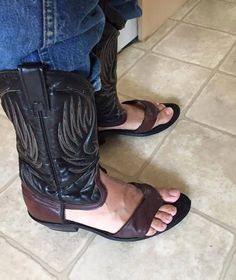 a person wearing cowboy boots and jeans standing on the floor with their feet in sandals