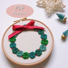 an embroidery hoop with green and red flowers on it, next to a small christmas tree ornament