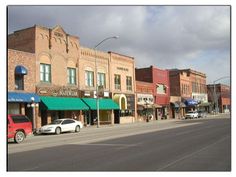 an empty city street with cars parked on the side and buildings in the back ground