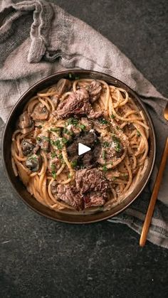 a bowl filled with pasta and meat on top of a table next to a wooden spoon