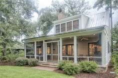 a house that is in the middle of some trees and grass with bushes around it