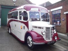 an old red and white bus parked in front of a brick building on the street