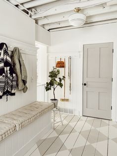 a white room with a bench, coat rack and potted plant