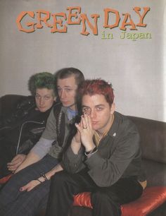 three young men sitting on a couch in front of a sign that reads green day in japan