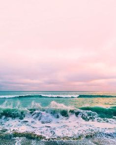 an ocean view with waves crashing on the shore and pink sky in the back ground