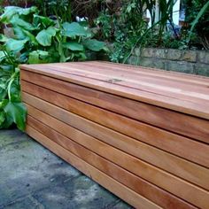 a large wooden box sitting on top of a cement ground next to green plants and bushes