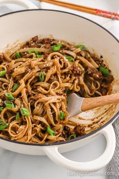 a skillet filled with noodles, meat and green onions next to chopsticks