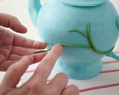 two hands reaching towards a teapot shaped like a plant on top of a table