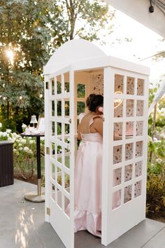 a woman in a pink dress standing inside of a white phone booth