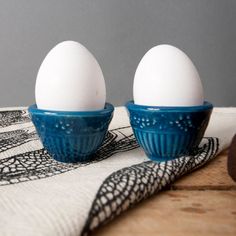 two eggs are sitting in blue bowls on a white towel next to an egg holder