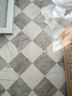 a white toilet sitting next to a wooden cabinet in a bathroom on top of a tiled floor