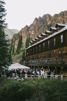 a group of people standing in front of a wooden building with mountains in the background