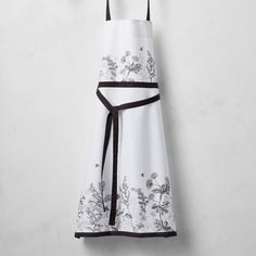 a white and black apron hanging from a hook on a wall with an embroidered flower design