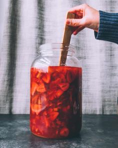 a person holding a wooden spoon in a jar filled with pickled carrots