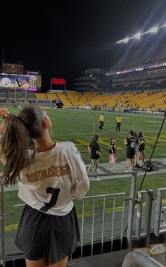 a girl is standing on the bleachers at a football game and looking up into the sky