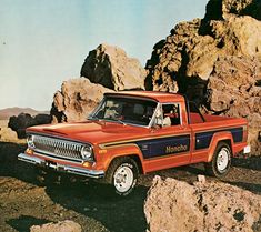 an orange pickup truck parked in front of some rocks