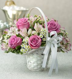 a basket filled with pink roses and white daisies on top of a table next to a silver vase