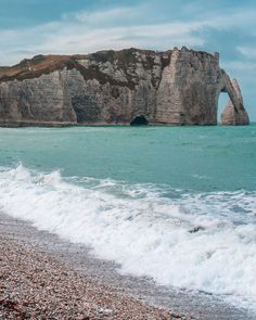 an ocean beach with waves crashing on the shore and a large rock formation in the distance