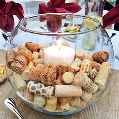 a glass bowl filled with wine corks and a lit candle on top of a table