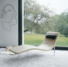 a lounge chair sitting in front of a window with a book on the floor next to it