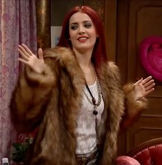 a woman with red hair wearing a fur coat and holding her hands up in the air