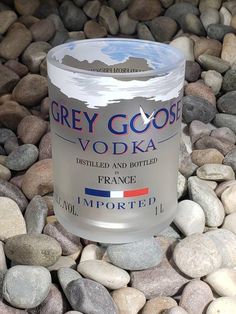 a can of grey goose vodka sitting on top of some rocks next to water and gravel