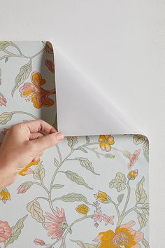 a hand is holding an envelope in front of a wallpapered background with flowers