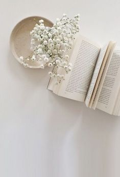 an open book with white flowers on it next to a small bowl filled with baby's breath