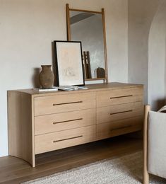 a wooden dresser sitting next to a white chair and a mirror on top of it